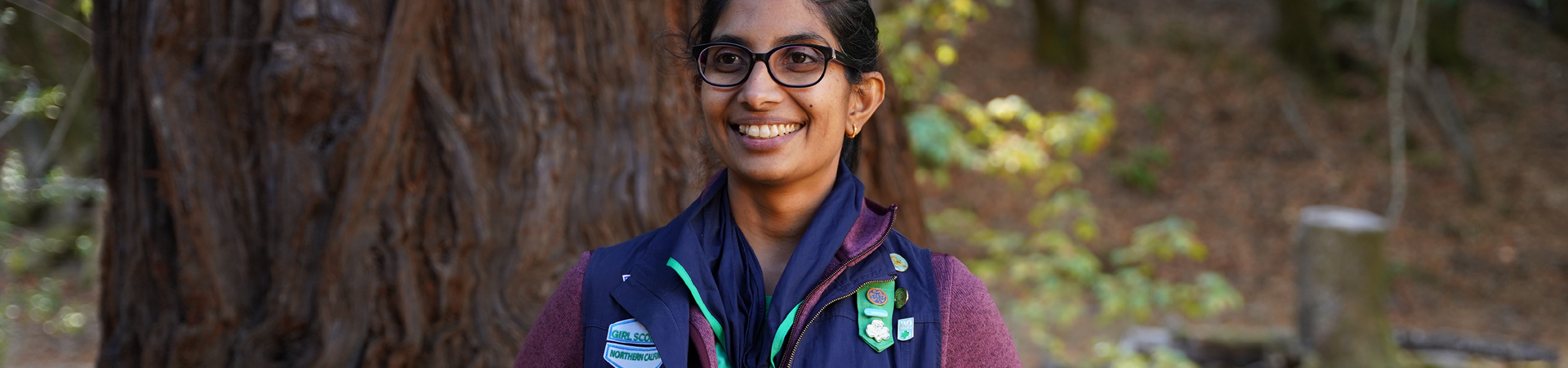  adult woman girl scout volunteer wearing vest outdoors with junior girl scout hiking 