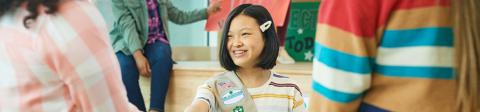  cadette girl scout hosting a table and smiling at a civics event with other middle school and high school girls  